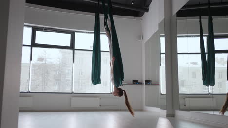 A-young-beautiful-woman-performs-exercises-on-a-hammock-from-aero-yoga.-A-woman-in-the-afternoon-in-front-of-the-mirror-in-the-hall-performs-stretching-alone